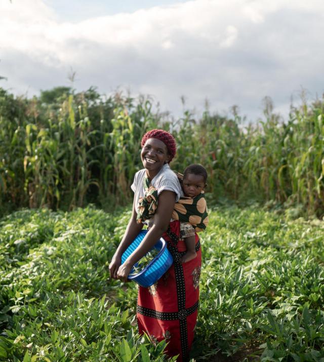 Photo of a woman carrying a child standing in a field.