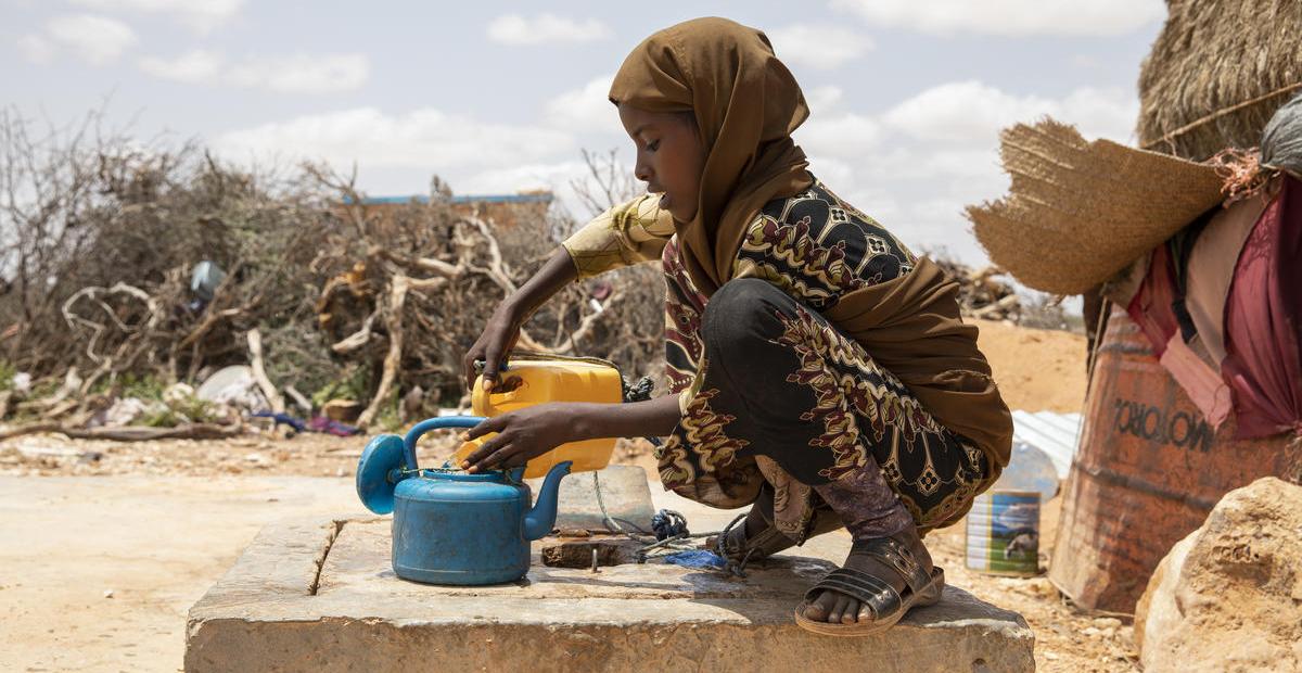 A young girl fills a kettle with water from a well.