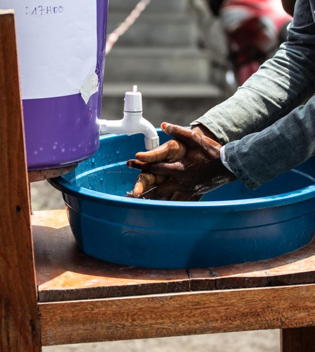 A photo of a person washing their hands over a plastic basin from a water jug.