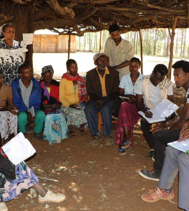A group of men and women sit in a circle at a meeting outside in Ethiopia