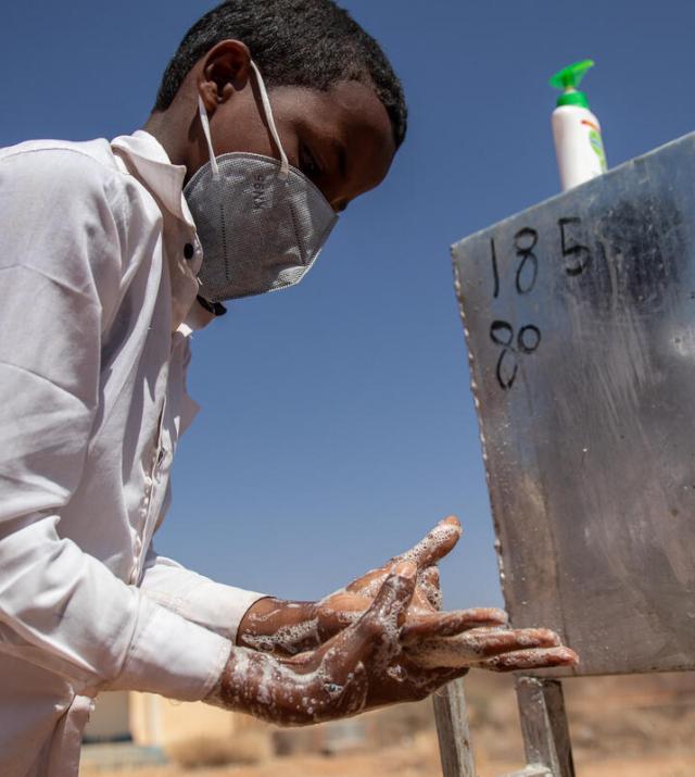 A young boy wearing a mask washes his hands at a handwashing station