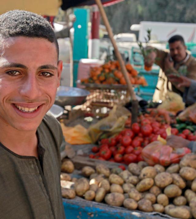 A young man stands in front of a stall selling fresh produce