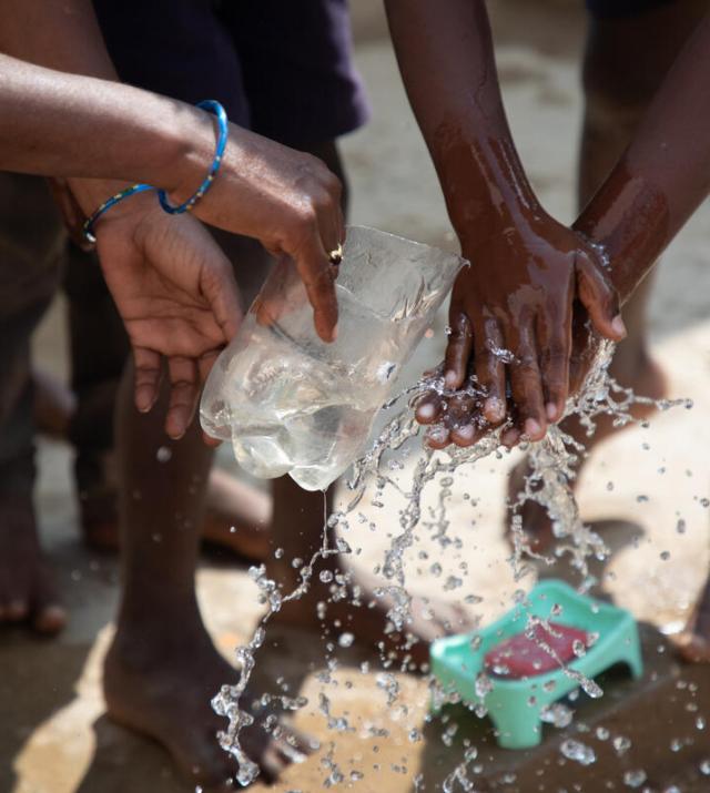 Children washing their hands using a plastic water bottle converted into a scoop.