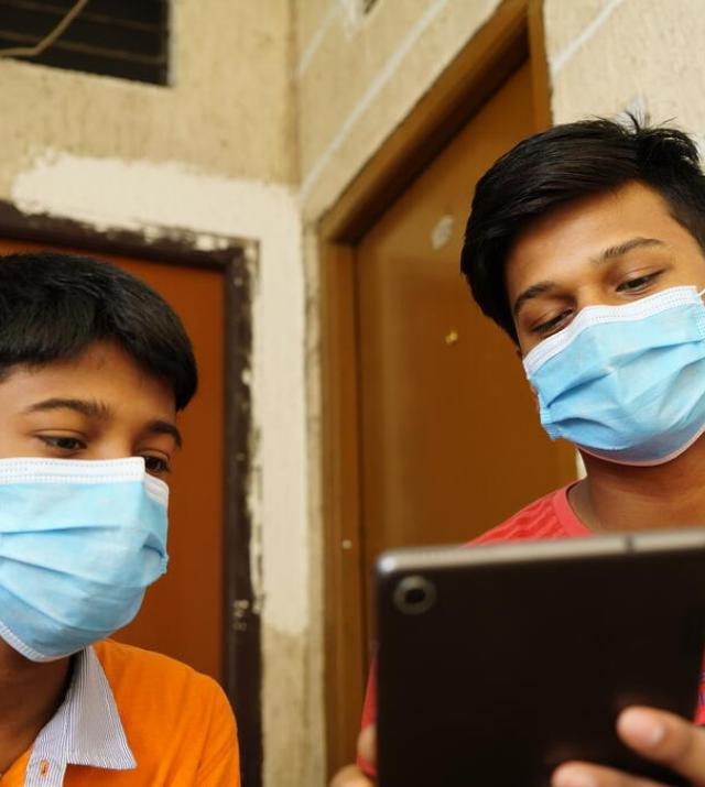 Two young men wearing face masks look at a tablet screen.