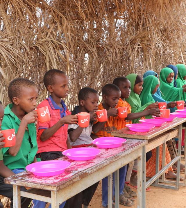 A group of children sit at their desks drinking tea awaiting a meal to be served.