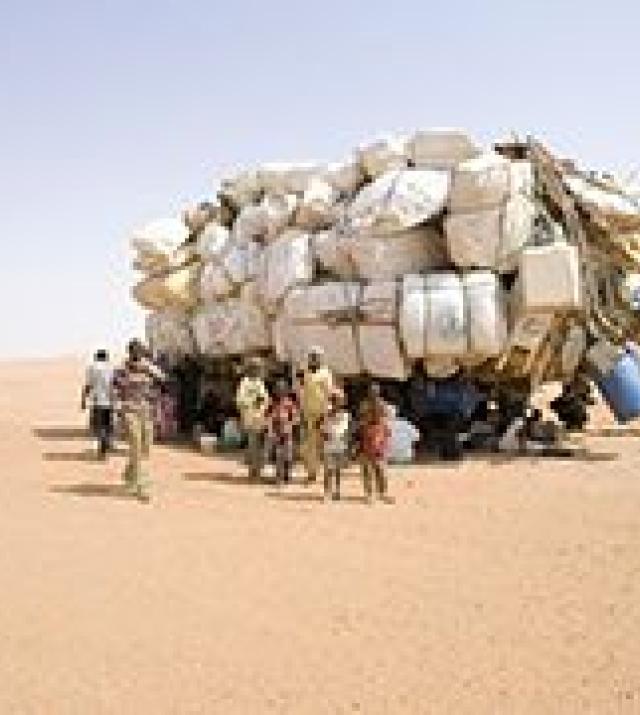 A truck loaded with white-wrapped items accompanied by people walking alongside it.