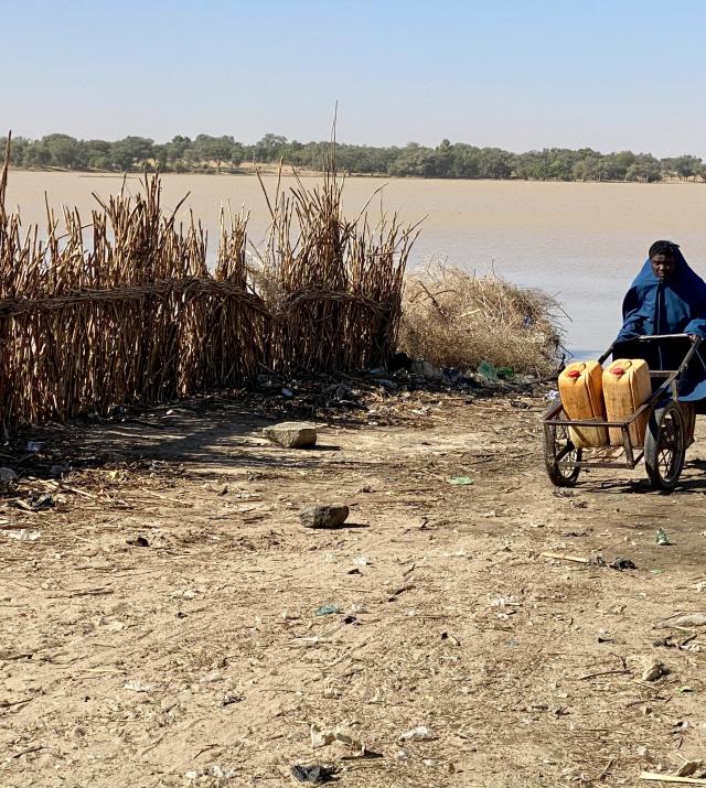 A person is transporting yellow buckets near a body of water