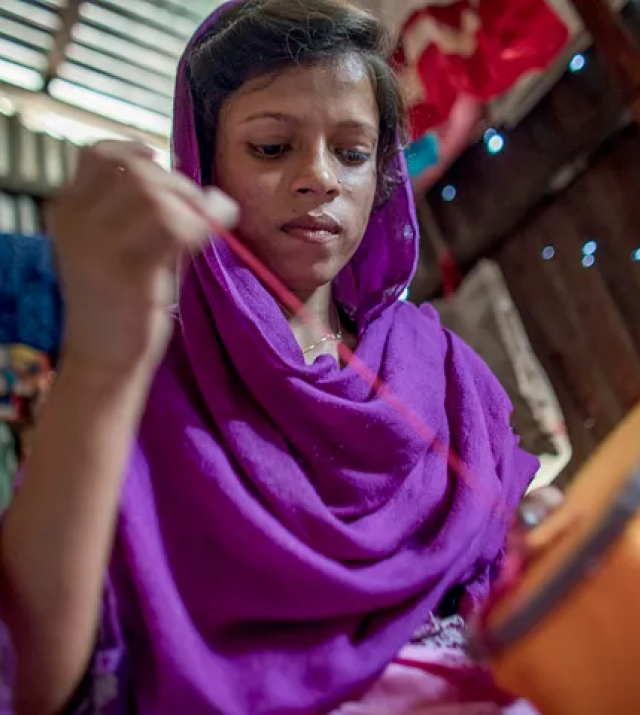 A young woman wearing purple pulls a needle and thread.