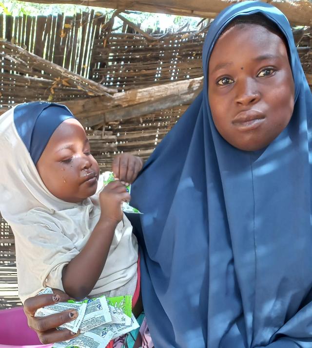 A woman wearing a blue headscarf holds her small child in her arms.