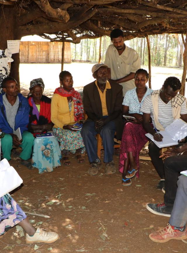 Un groupe d'hommes et de femmes sont assis en cercle lors d'une réunion à l'extérieur en Éthiopie