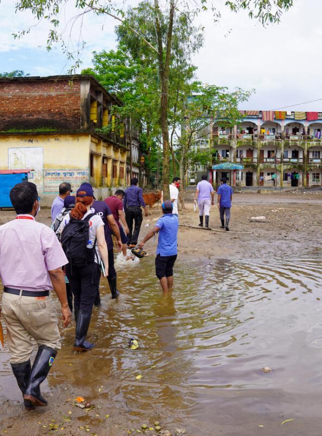Un groupe de personnes marche dans les eaux d'une inondation vers un ensemble de bâtiments