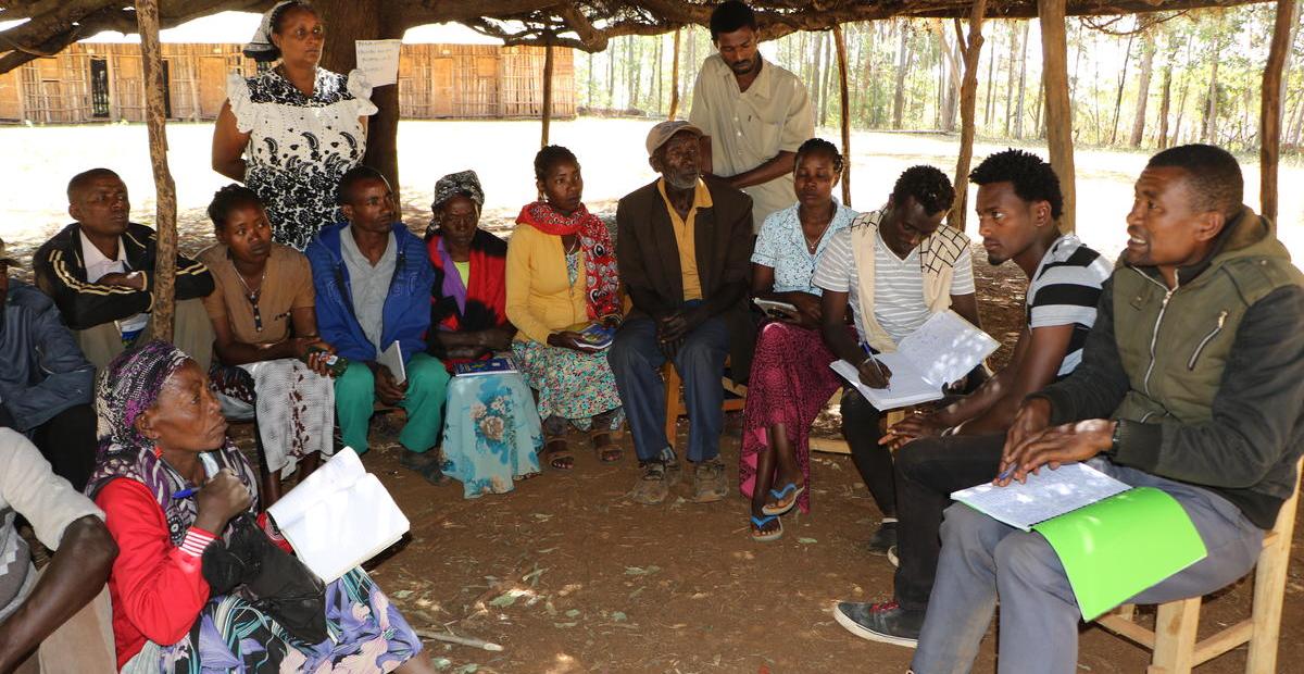Un groupe d'hommes et de femmes sont assis en cercle lors d'une réunion à l'extérieur en Éthiopie
