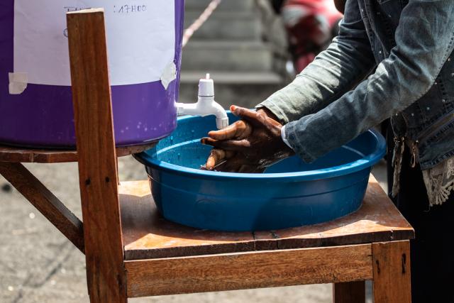 A photo of a person washing their hands over a plastic basin from a water jug.