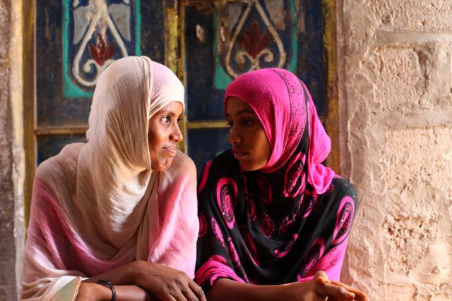 Two Yemeni women sitting side-by-side, looking at one another