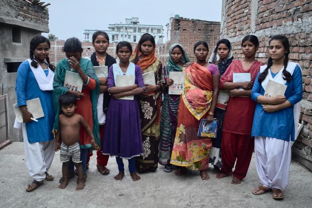 Photo of a group of women standing in a row holding educational materials