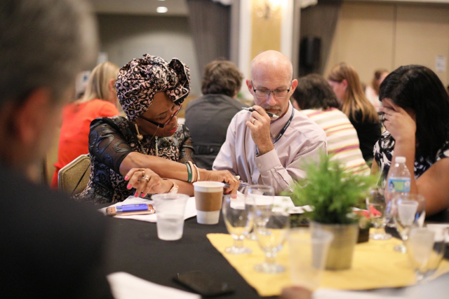 Three people sitting around a table at a conference reading a document