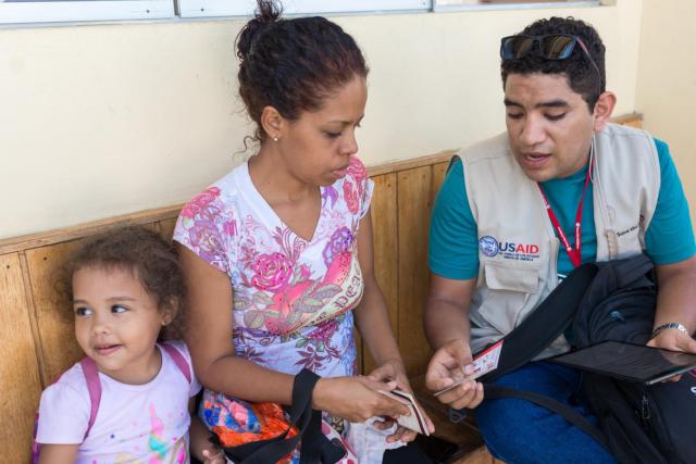 Project worker showing a woman who is sitting next to her child how to use a voucher.