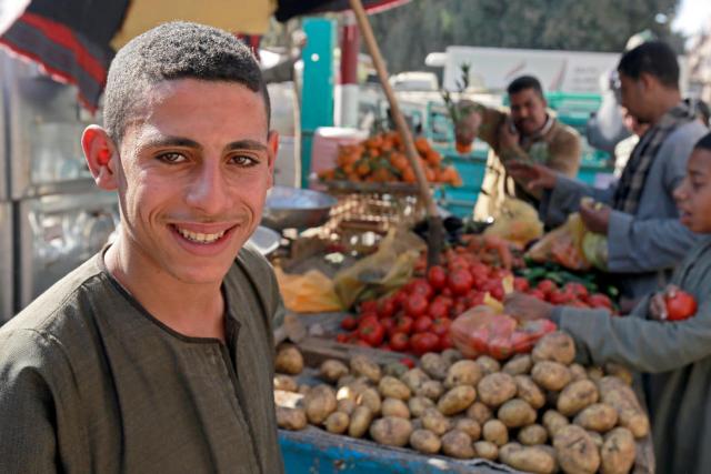 A young man stands in front of a stall selling fresh produce