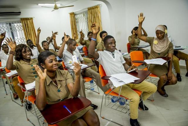 Students in a classroom raise their hands while seated.