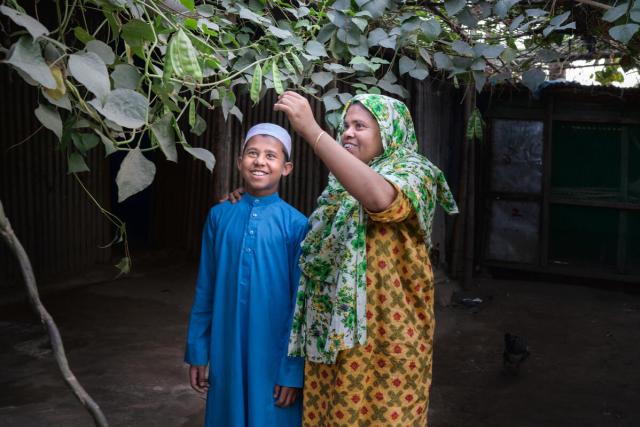 A boy and a women smile looking at a plant tree
